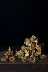 Obraz premium Hazelnuts with husks and shells on rustic wooden board with black background and negative space.