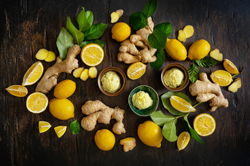 Homemade lemon and ginger ice cream in ceramic cups and fresh fruit and lemon leaves and ginger roots on a dark wooden background. Cold summer dessert concept. Top view