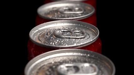 A lot of red cans dolly footage above droplets of water on bottle. Black background. The concept of a production or can factory.