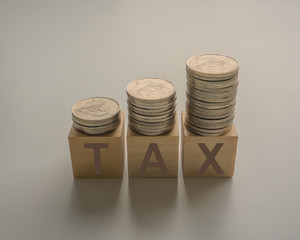 Tax concept with stacked coins on wooden cube
