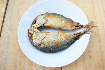 2 fried mackerel in a white plate on wooden background.