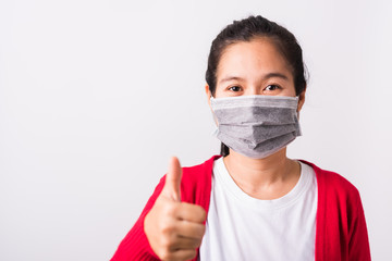 Asian adult woman wearing red shirt and face mask protective against coronavirus or COVID-19 virus or filter dust, air pollution her show finger thumb up for good sign, isolated white background