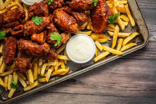 Overhead Shot Of Buffalo Wings With Sauce And Fries On A Tray On Wooden Table