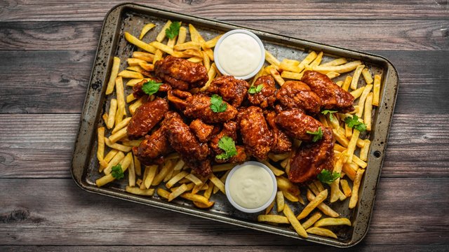 Overhead Shot Of Buffalo Wings With Sauce And Fries On A Tray On Wooden Table