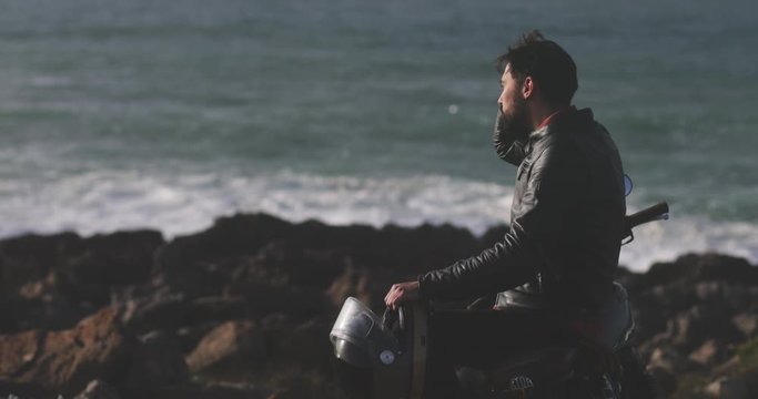 Handsome man wearing leather jacket on motorcycle by the seafront