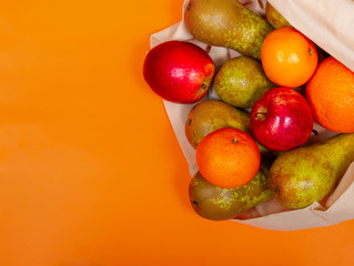 Ecology concept: fruits (pears, apples, oranges) in a cotton shopping bag on orange backgrond. Top view. Copy space