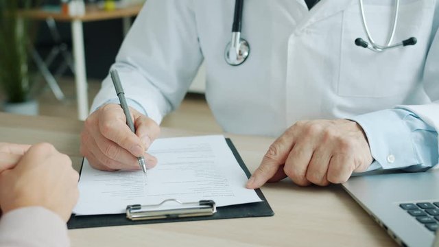 Close-up of male doctor filling in medical chart talking to female patient in office writing and ticking answers collecting symptoms. Medicine and healthcare concept.