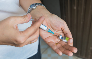 Hand with syringe draw vaccine from vial.