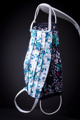 Desktop LED light with two homemade face masks resembling surgical medical mask with pattern of the original cloth hanging from it. Studio low key product still life.