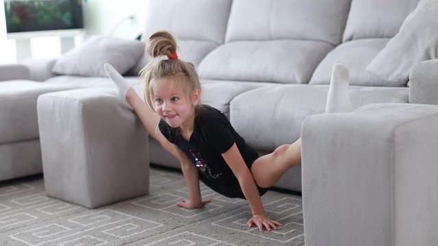 Little cute girl is practicing gymnastics at home. Online training. Stretching, twine. Quarantine. Stay at home.