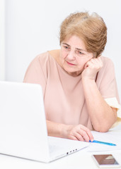 Sad senior woman looks at laptop in the office