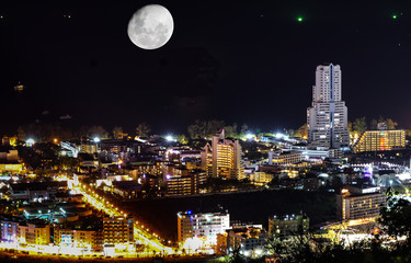 Patong Phuket Thailand night time long expose photograph with the night skyline illuminated by the city lights and the moon over the Andaman sea and Patong Bay