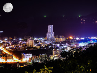 Patong Phuket Thailand night time long expose photograph with the night skyline illuminated by the city lights and the moon over the Andaman sea and Patong Bay