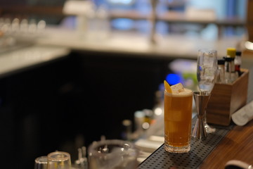 a glass of orange color cocktail on bar counter at night. blur dark background