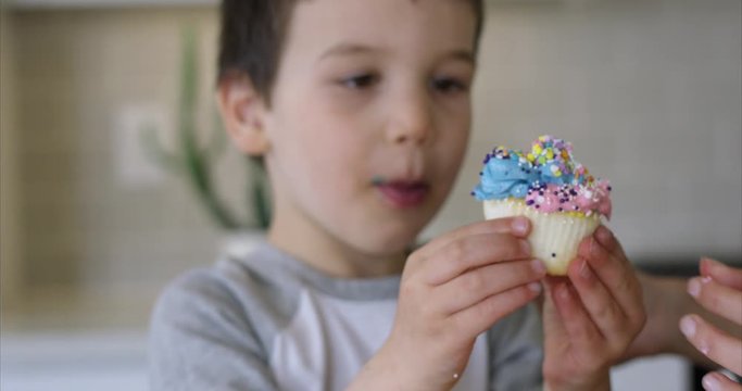 Toddler boy takes fancy cupcake from others hand and eats it - close up on face - slow motion