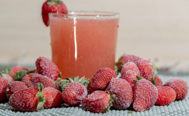Frozen fresh strawberries and strawberry juice on a light and blurred background