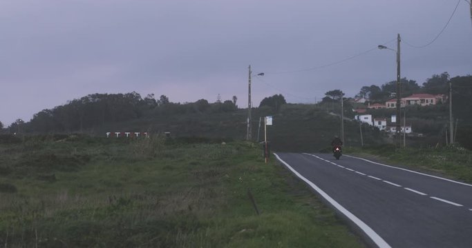 Biker man riding off on classic motorcycle on country road