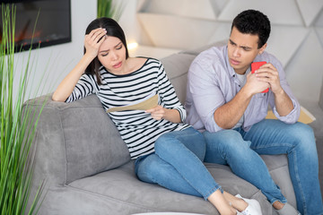 Anxious woman with letter, a husband next with smartphone.