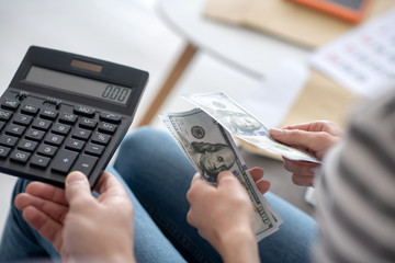 Fototapeta premium Male hand holding a calculator, female hands with dollar bills.