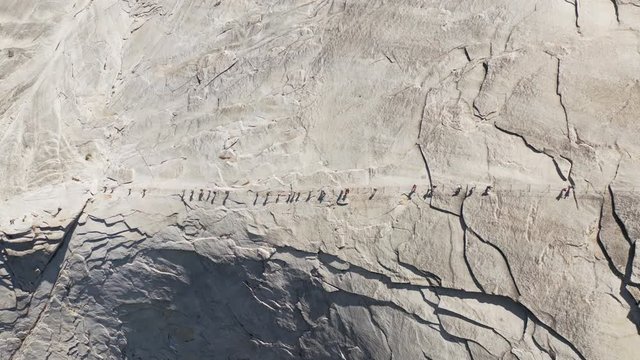 Top aerial footage of a group of tourists climbing a specially equipped trail which goes up a smooth stone slope to the top of the famous Half Dome mountain, located in Yosemite National Park, USA. 4K