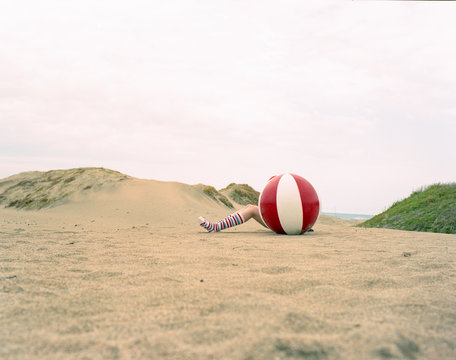 Low section of woman hiding behind ball on beach