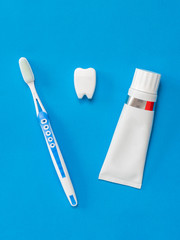 Figure of a tooth between a toothpaste and a brush on a blue background. Flat lay.