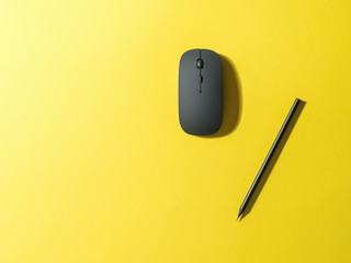 Black mouse and black pencil on a bright yellow background.