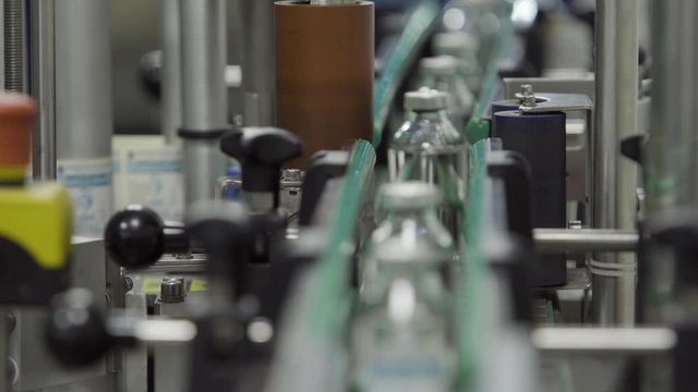 glass bottles filled and sealed with rubber and aluminum caps on labelstock area of medical solution conveyor line close up selective focus medical industry