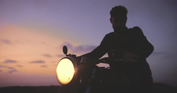 Close up man riding off during sunset on classic motorcycle