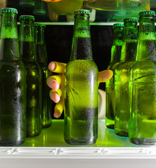 The hand reaches for the beer bottle. Green bottles of beer and drops of condensation are on a...