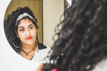 Girl near mirror. Curvy brazilian woman with red lips with love looks at herself. Body positive or...