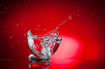 A splash of a drink in a glass, shot against a bright red background.