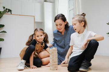 Mom and children playing popular game with wooden blocks, building high tower