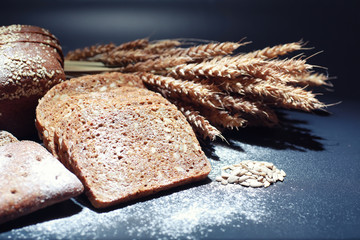 Fresh loaves of bread with wheat and gluten on a black table. Bakery and grocery concept. Fresh, healthy sorts of rye and white loaves food closeup. Fresh homemade bread with cereals.