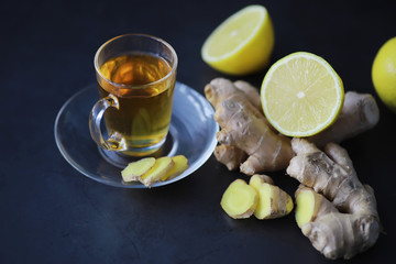 Ginger root whole and sliced. Ginger tea with lemon on the dark background. Fresh ginger root on stone background. Vitamins. Free space for your text.