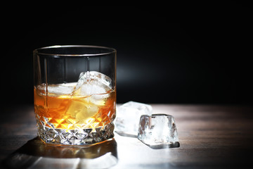A glass of strong alcoholic drink with ice on a wooden bar counter. Whiskey with ice cubes. Glass...