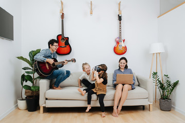 Parents and kids having good tome on a sofa, eash doing his or her own thing
