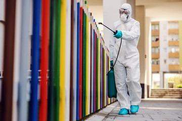 Man in sterile uniform and mask sterilizing fence of kindergarten from covid-19 / corona virus.
