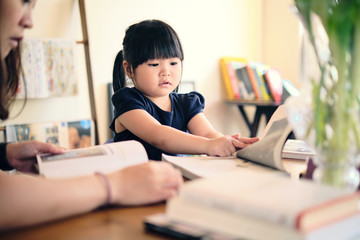 Cute asian girl with mother learning by reading and studying books and playing at home in the living room, home schooling education for children, feeling happy cheerful, and enjoying staying at home