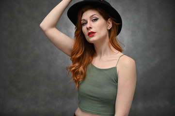 Naklejka premium Woman shows emotions changing poses. Portrait of a young pretty girl with beautiful hair and great makeup in a green T-shirt and black hat on a gray background.