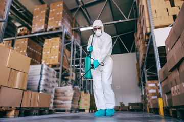 Naklejka na ściany i meble Man in protective suit and mask disinfecting warehouse full of food products from corona virus / covid-19.