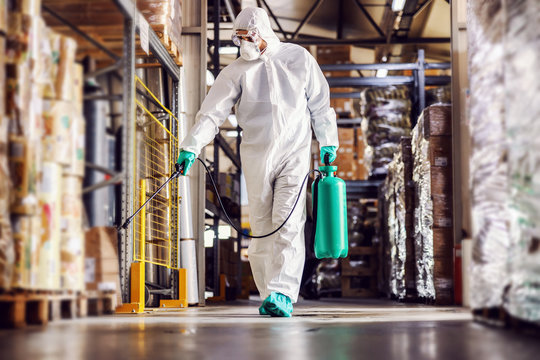 Man in protective suit and mask disinfecting warehouse full of food products from corona virus / covid-19.