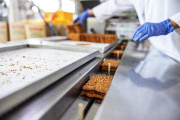 Closeup of worker picking up biscuits form machine while standing in food factory.