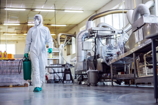 Man in protective suit and mask disinfecting food factory full of food products from corona virus / covid-19.