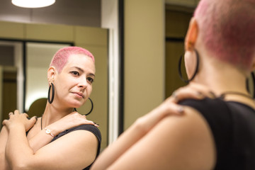 Healthy woman after chemotherapy looks in mirror at herself with love and hope. Girl with short...