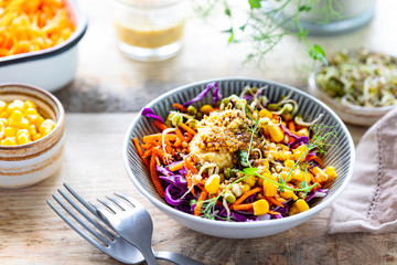 Vegetable salad of fresh red cabbage with carrots, onions, corn, mung seedlings in a plate on wooden background. Selective focus.