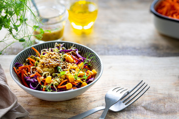 Vegetable salad of fresh red cabbage with carrots, onions, corn, mung seedlings in a plate on wooden background. Selective focus. Copy space. horizontal