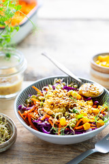 Vegetable salad of fresh red cabbage with carrots, onions, corn, mung seedlings in a plate on wooden background. Selective focus. Copy space. Vertical