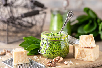 Wild leek pesto with olive oil and parmesan cheese in a glass jar on a wooden table. Useful...
