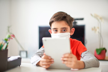 niño aprendiendo en casa con dispositivo electrónico con mascarilla